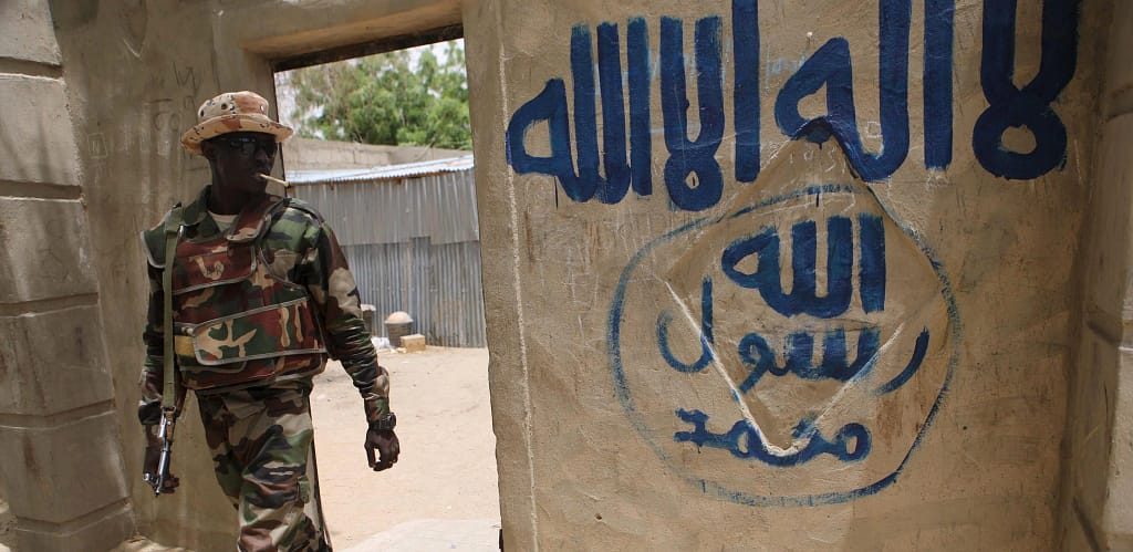 Armed militant walks past graffiti associated with ISIS inside a damaged building in northern Nigeria