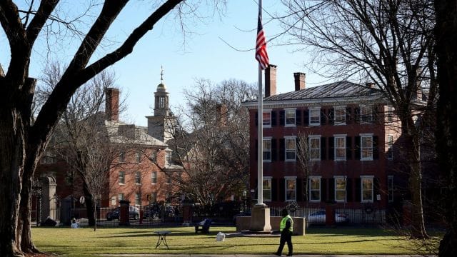 A security guard walks past a flag at half-staff on the main green of Brown University in Providence, RI, Thursday, Dec. 18, 2025, (AP Photo/ Mark Stockwell)