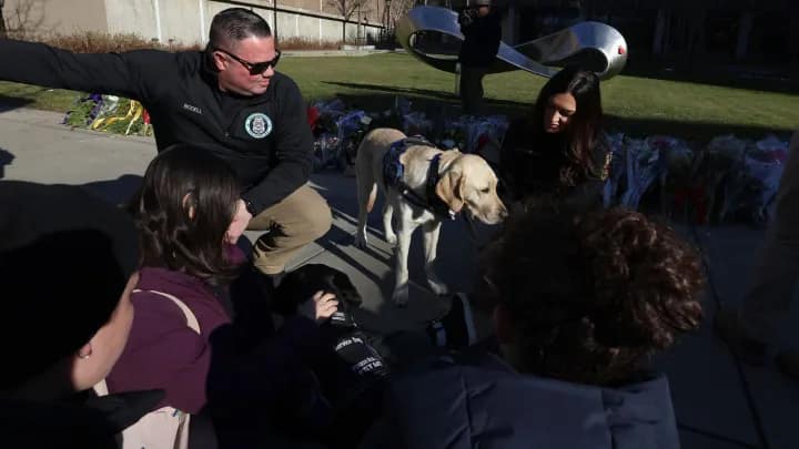Middletown, CT, community police officer Jason Bodell and his comfort dog, Bear, meet with visitors at a memorial in front of the Barus and Holley engineering building on the campus of Brown University in Providence, Thursday, Dec. 18, 2025. (AP/ Mark Stockwerll)